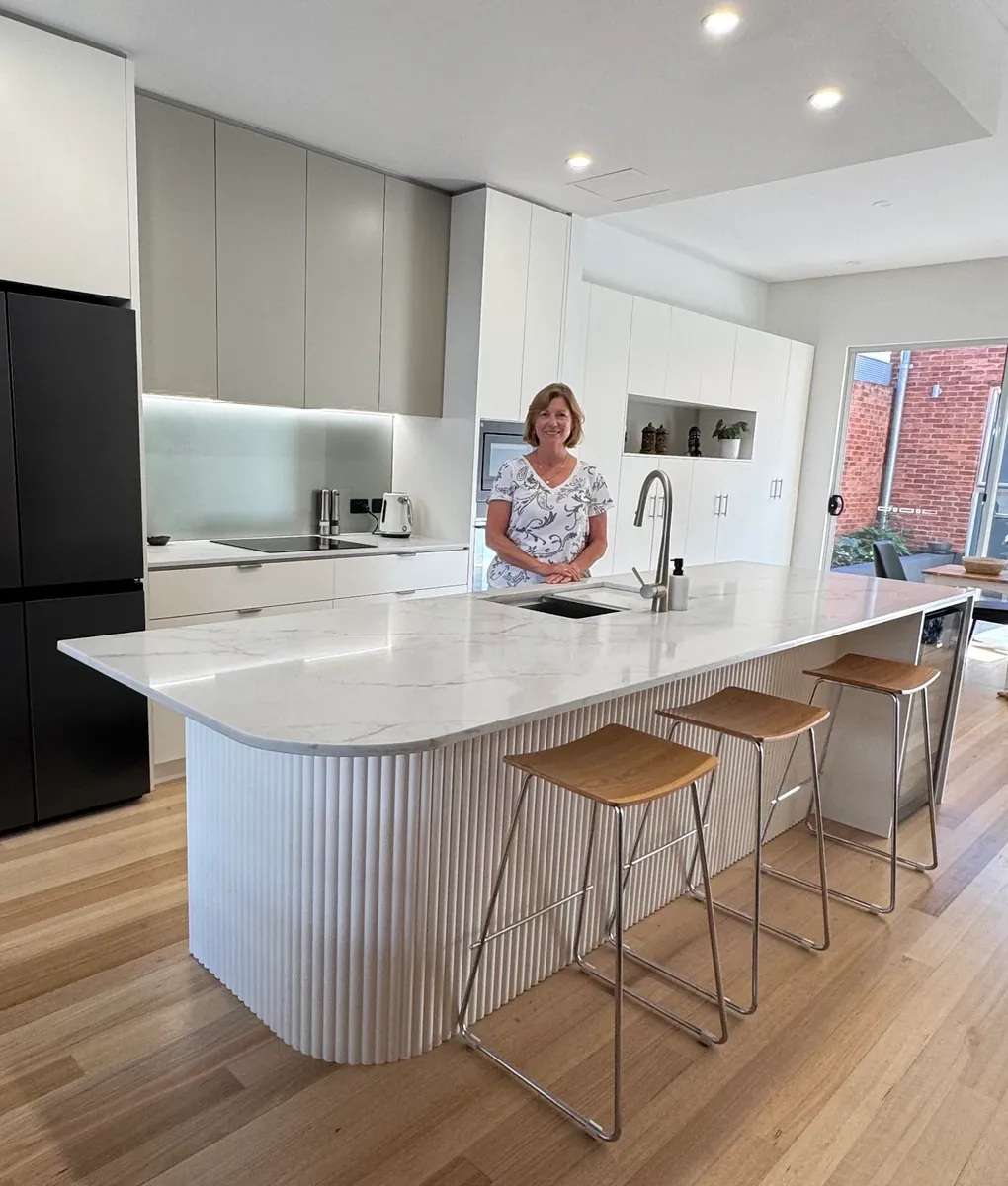 A client standing in a bright modern kitchen with a marble island bench and custom joinery