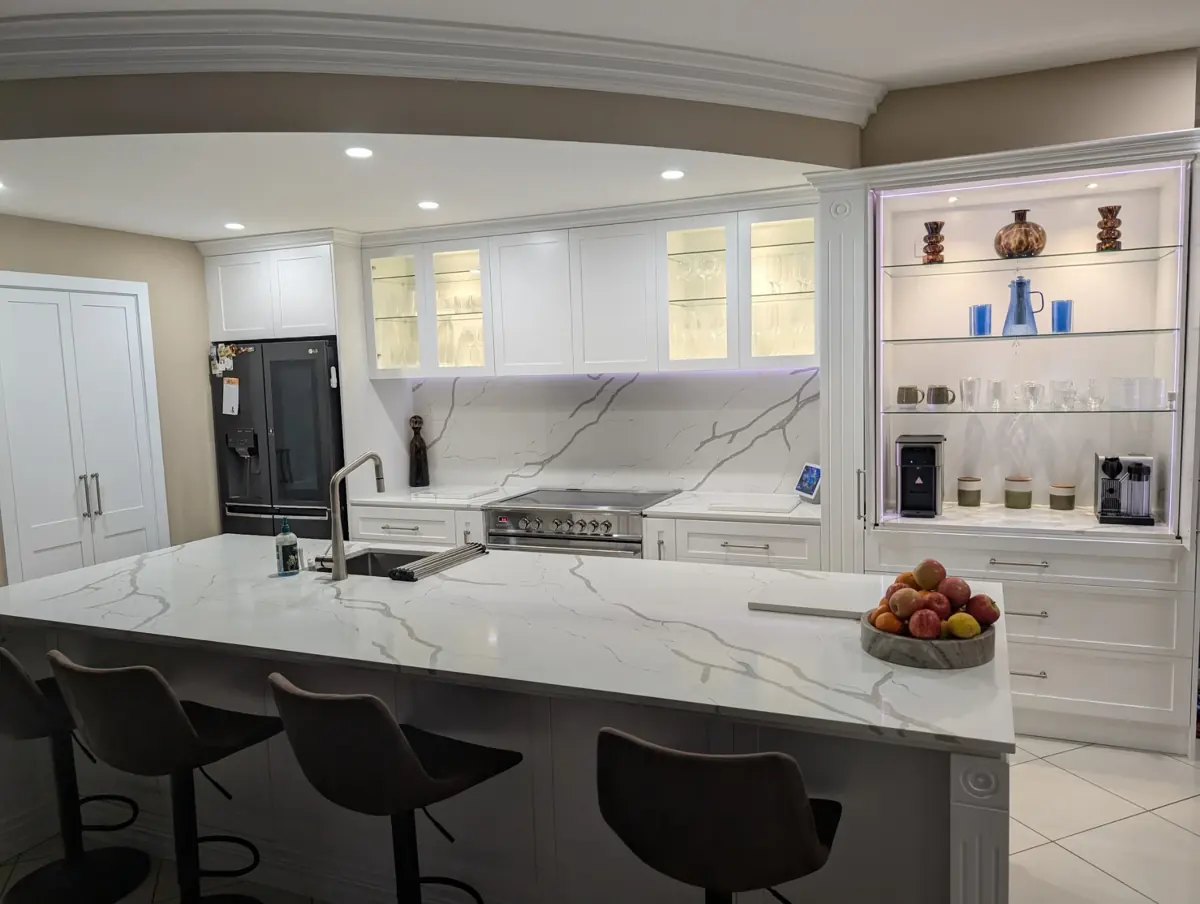 A classic white kitchen with marble-look stone benchtops, glass display cabinetry and feature lighting