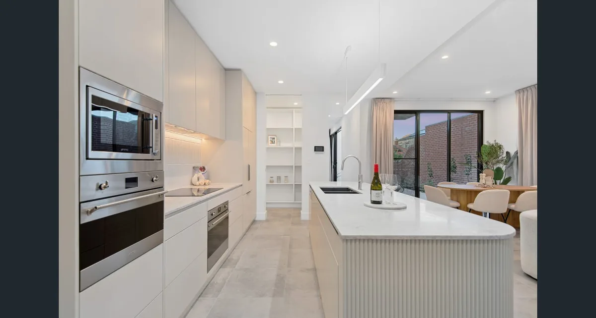 A contemporary white kitchen with a ribbed island bench, integrated appliances and open-plan dining