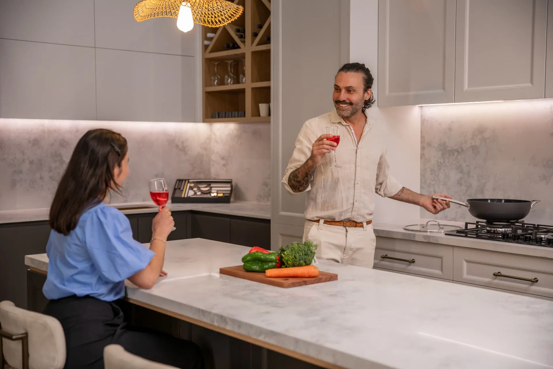 A couple enjoying drinks in a custom Haute Kitchen with stone island bench and warm lighting