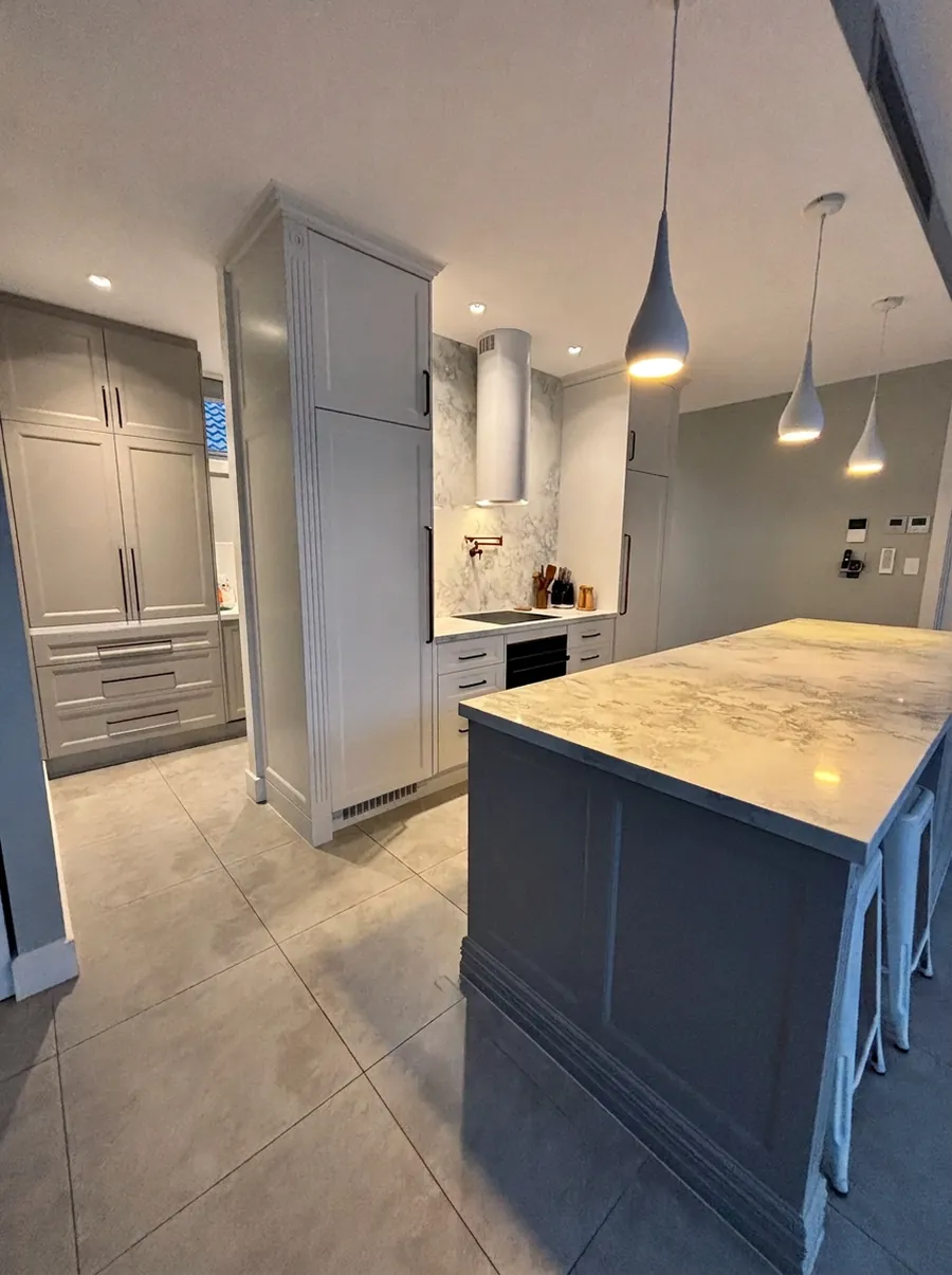 A light grey shaker kitchen with a dark island, marble-look benchtops, teardrop pendant lights and integrated tall cabinetry