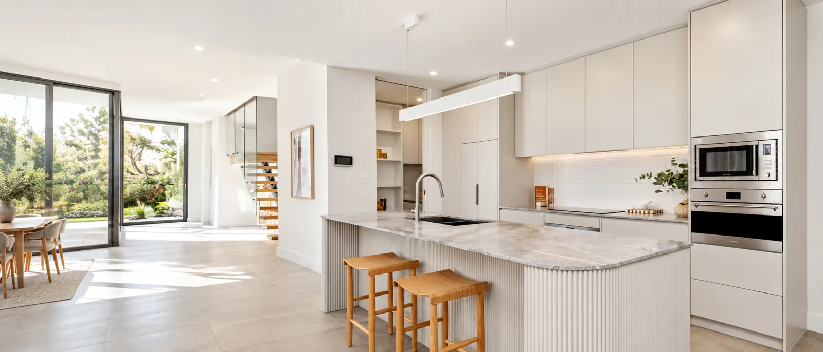 A bright custom Haute Kitchen with white cabinetry, stone island bench and timber stools
